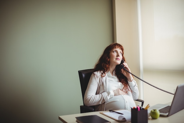 Free photo pregnant businesswoman touching her belly while talking on telephone