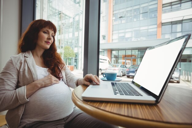 Pregnant businesswoman using laptop in cafeteria