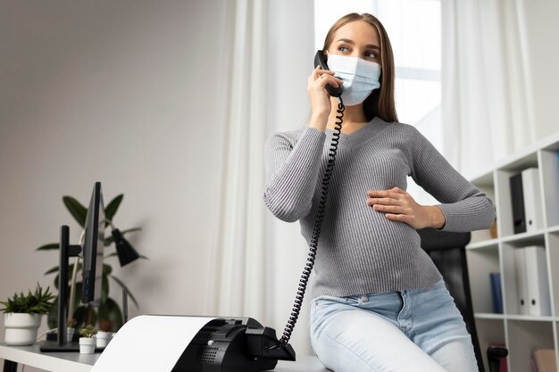 Pregnant businesswoman with medical mask taking calls in the office