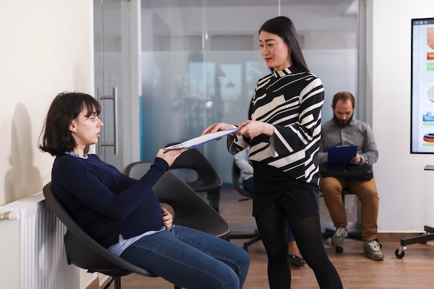 Pregnant candidate giving cv documents to entrepreneur woman during interview meeting in startup company office. Asian businesswoman recruiting employer for human resources job. Hiring process concept