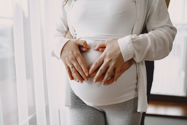 Беременная в легкой одежде. Руки на животе беременной женщины. Семья у окна.