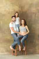 Free photo pregnant mother with teen daughter and husband. family studio portrait over brown background