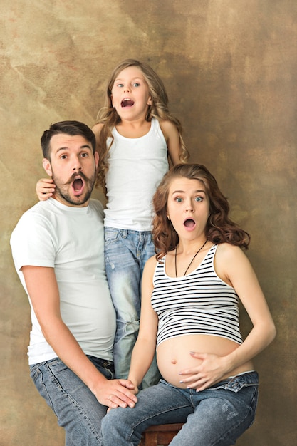 Free photo pregnant mother with teen daughter and husband. family studio portrait over brown wall