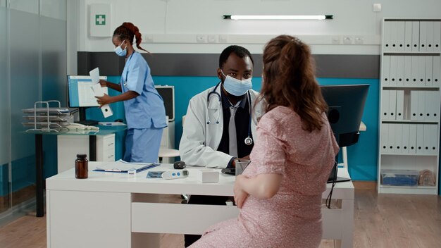 Pregnant patient meeting with doctor in cabinet during covid pandemic