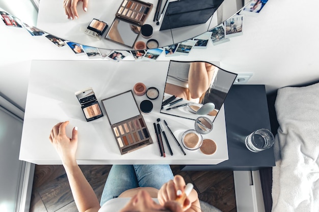 Free photo a pregnant woman applies makeup at home in front of a mirror