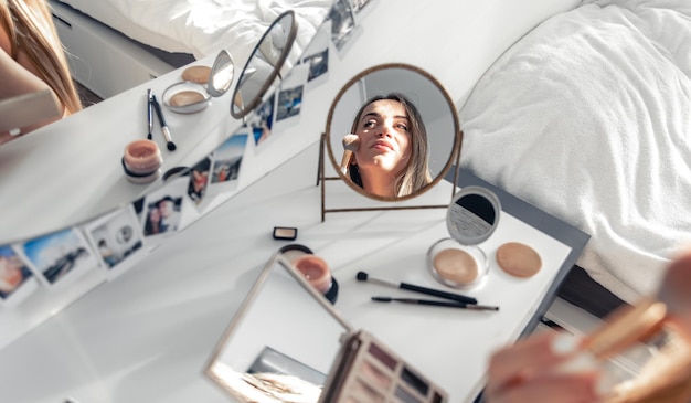 Free photo a pregnant woman applies makeup at home in front of a mirror