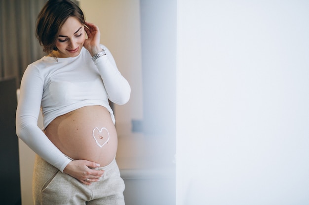 Беременная женщина наносит крем на живот для предотвращения растяжек