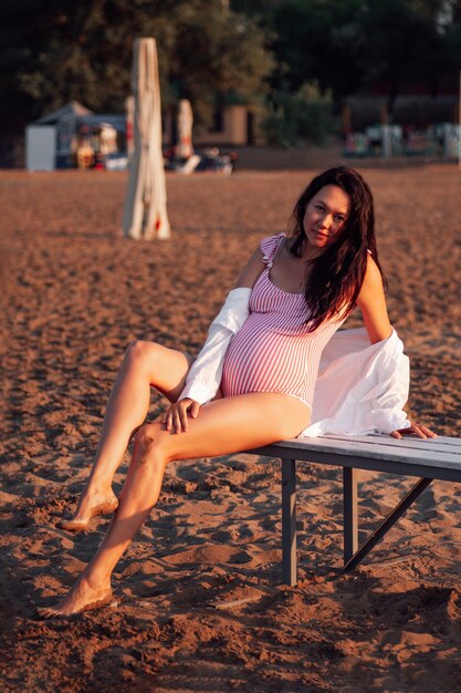 Pregnant woman on the beach fulllength portrait of a brunette pregnant woman in a pink swimsuit posi...
