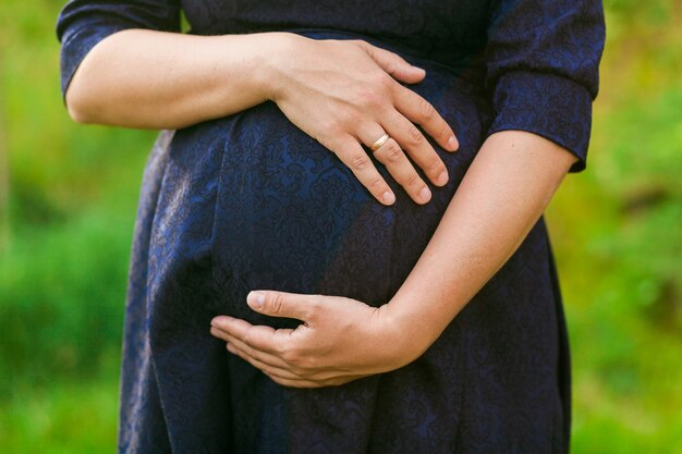 blured緑の草の背景に黒い服を着た妊婦