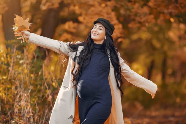 秋の公園で茶色のコートで妊娠中の女性