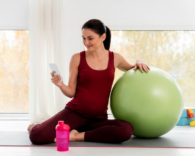 Беременная женщина проверяет свой телефон после тренировки