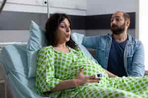 Free photo pregnant woman doing breathing exercices, holding hands on belly while having painful contractions. patient with pregnancy going into labor in hospital ward, husband standing beside her comforting.