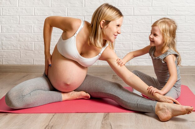 Pregnant woman doing fitness exercise with her little girl