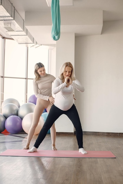 Donna incinta che fa yoga con personal trainer istruttore di yoga che assiste la donna incinta mentre fa esercizi donna incinta bionda che indossa abiti bianchi