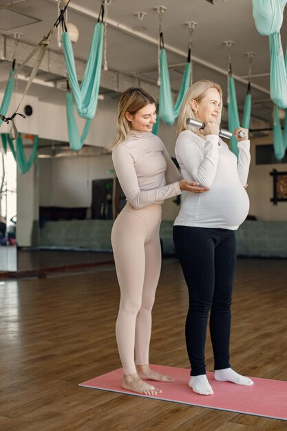 パーソナルトレーナーと一緒にヨガをしている妊婦フィットボールとダンベルでエクササイズをしながら妊婦を支援するヨガトレーナー白いシャツを着た金髪の妊婦