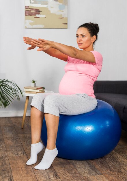 Беременная женщина, тренирующаяся дома с мячом