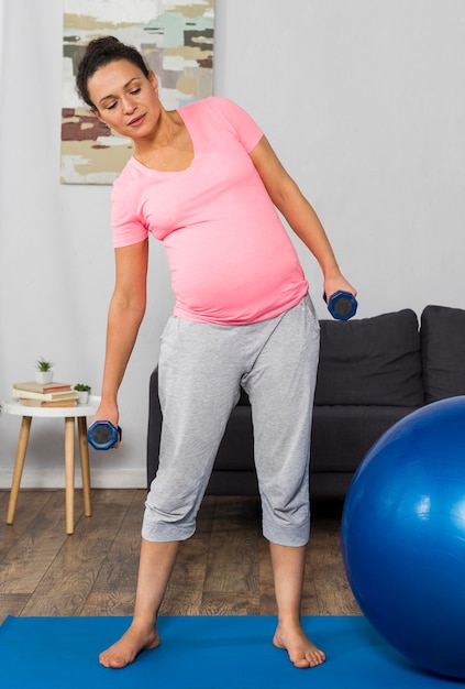 Pregnant woman exercising on mat at home with ball and weights