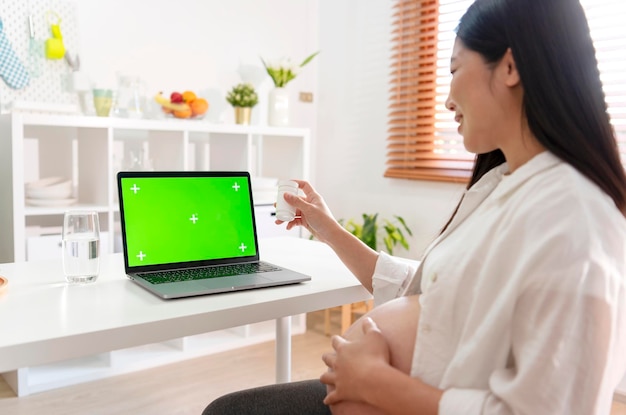Беременная женщина, имеющая онлайн-консультацию с врачом на ноутбуке дома, макет зеленого экрана