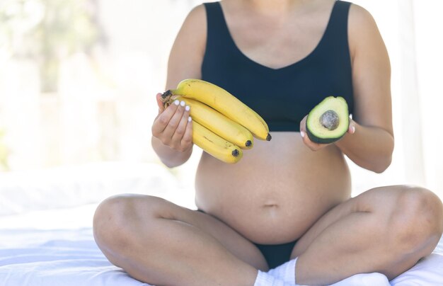 Pregnant woman holding avocado and bananas health and maternity concept