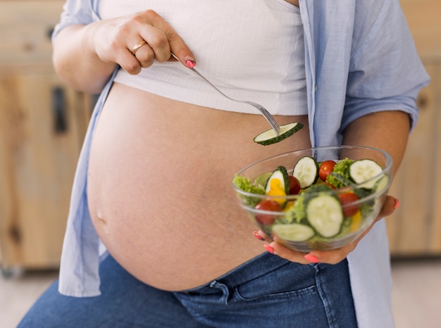Беременная женщина, держащая тарелку с салатом