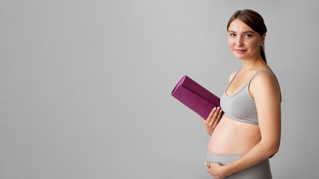 Pregnant woman holding a fitness mat with copy space