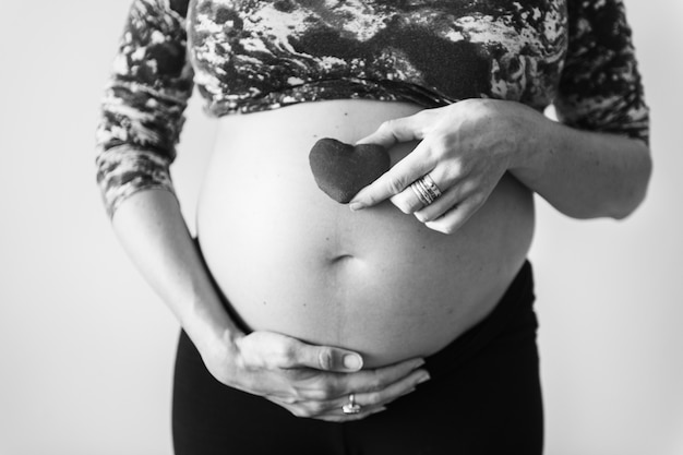 Foto gratuita donna incinta che tiene un cuore davanti al suo pancione