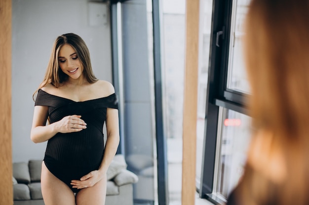 Free photo pregnant woman holding her belly and looking into the mirror