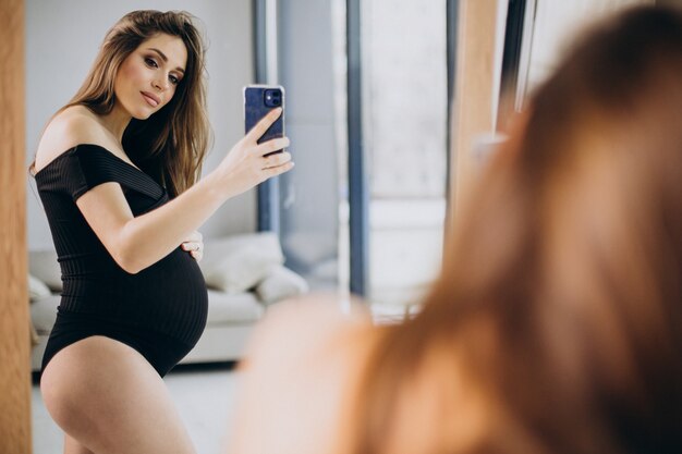 Pregnant woman holding her belly and looking into the mirror