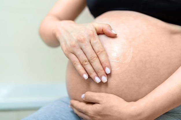 Pregnant woman holding her naked belly and rubbing the cream