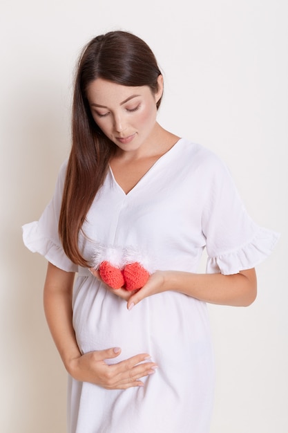 Pregnant woman holding knitted baby booties and looking at it