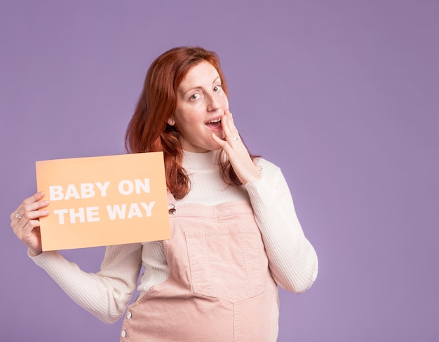 Pregnant woman holding paper with baby on the way message