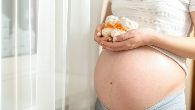 Pregnant woman holding small shoes on her naked belly