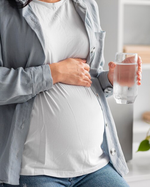 Беременная женщина дома, держа стакан воды