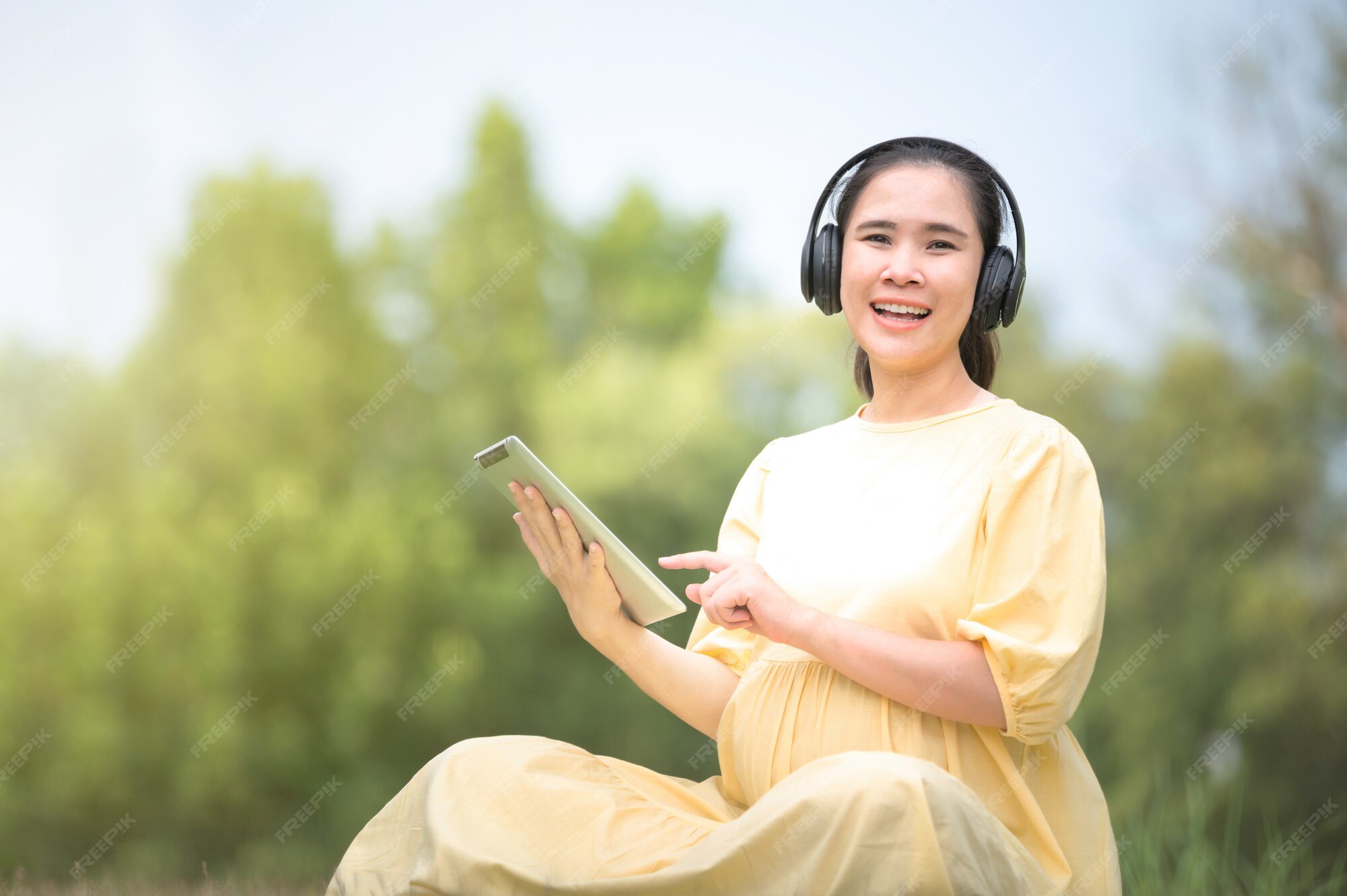 Premium Photo | A pregnant woman is relaxing in the park and listening to  music on a tablet, mom listening songs for the unborn child, pregnant near  giving birth, mother and child