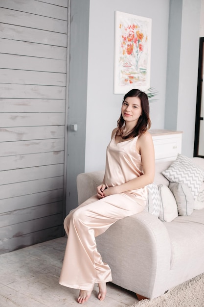 A pregnant woman is sitting on the couch in her pajamas at home Concept of rest and weekends