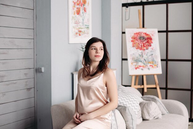 A pregnant woman is sitting on the couch in her pajamas at home Concept of rest and weekends