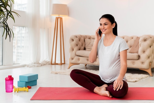 Free photo pregnant woman in lotus position talking on the phone with copy space