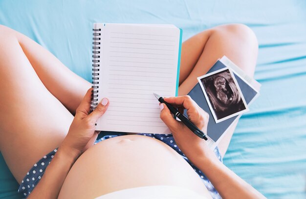 Pregnant woman makes notes in notebook and holding ultrasound image and medical documents Premium Photo