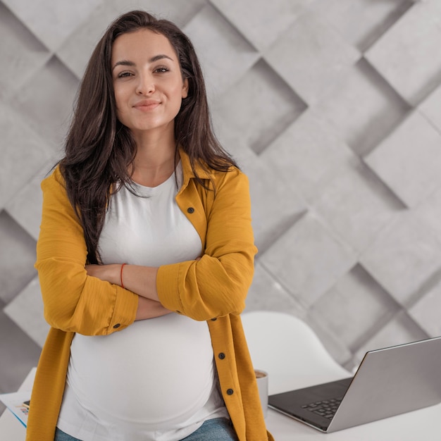 Foto gratuita donna incinta che posa con il computer portatile e la casa