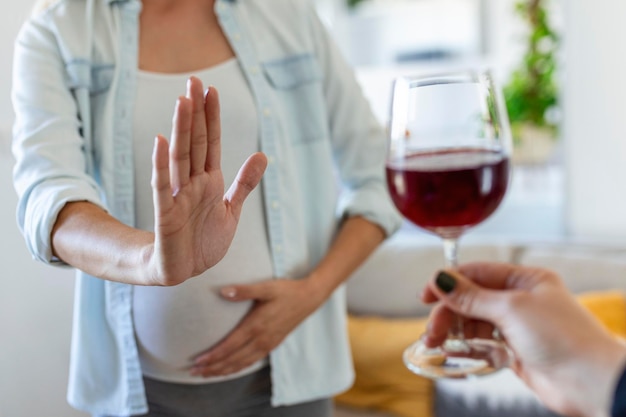 Free photo pregnant woman refusing a glass of wine alcohol in pregnancy unrecognizable expectant lady gestring stop to offered glass of wine