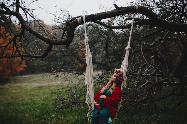 Pregnant woman rests outside on the rope swing hanging on old tr
