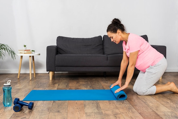 Pregnant woman rolling up exercising mat at home