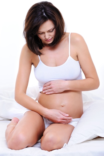 Pregnant woman sitting on bed and stroking her tummy