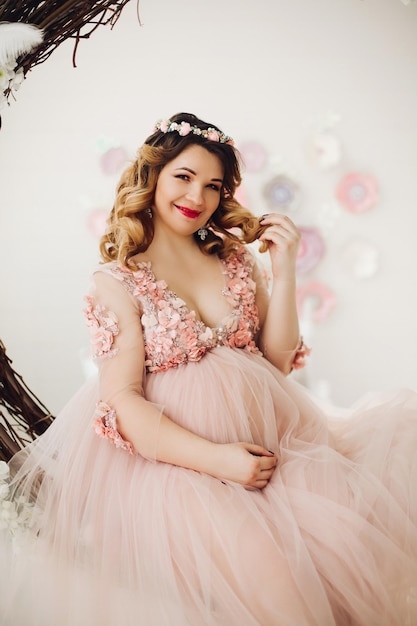 Free photo pregnant woman sitting on big decorated vine wreath