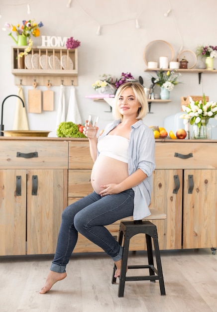 Free photo pregnant woman sitting on chair while holding a glass of water