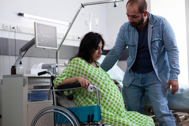 남편이 임신과 출산을 돕는 동안 휠체어에 앉아 있는 임산부. 시설에 의료 장비가 있는 병원 병동에서 아기와 출산 절차를 기다리는 부부