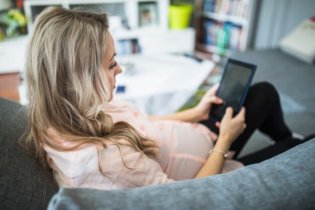 Pregnant woman sitting on sofa using digital tablet