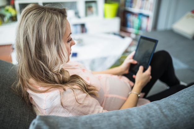 Pregnant woman sitting on sofa using digital tablet