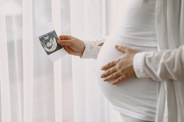 Pregnant woman standing by the window looking at a photo.