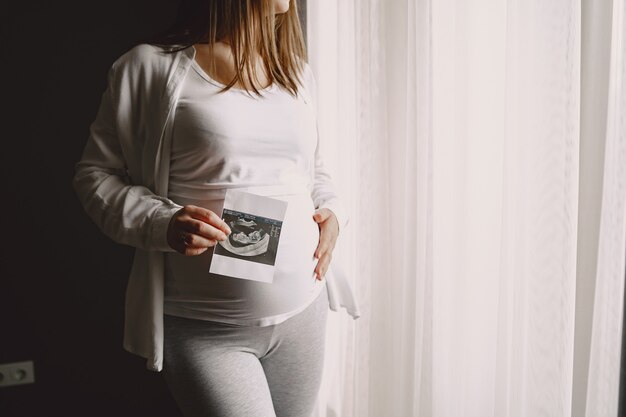 写真を見ている窓際に立っている妊婦。